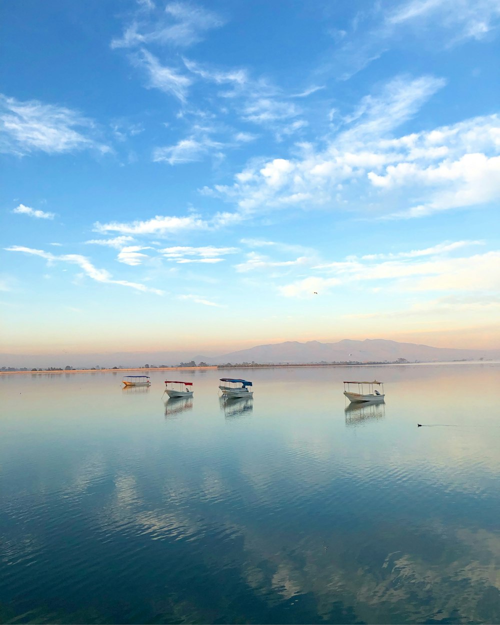 four boats on body of water under blue sky and white clouds during daytime