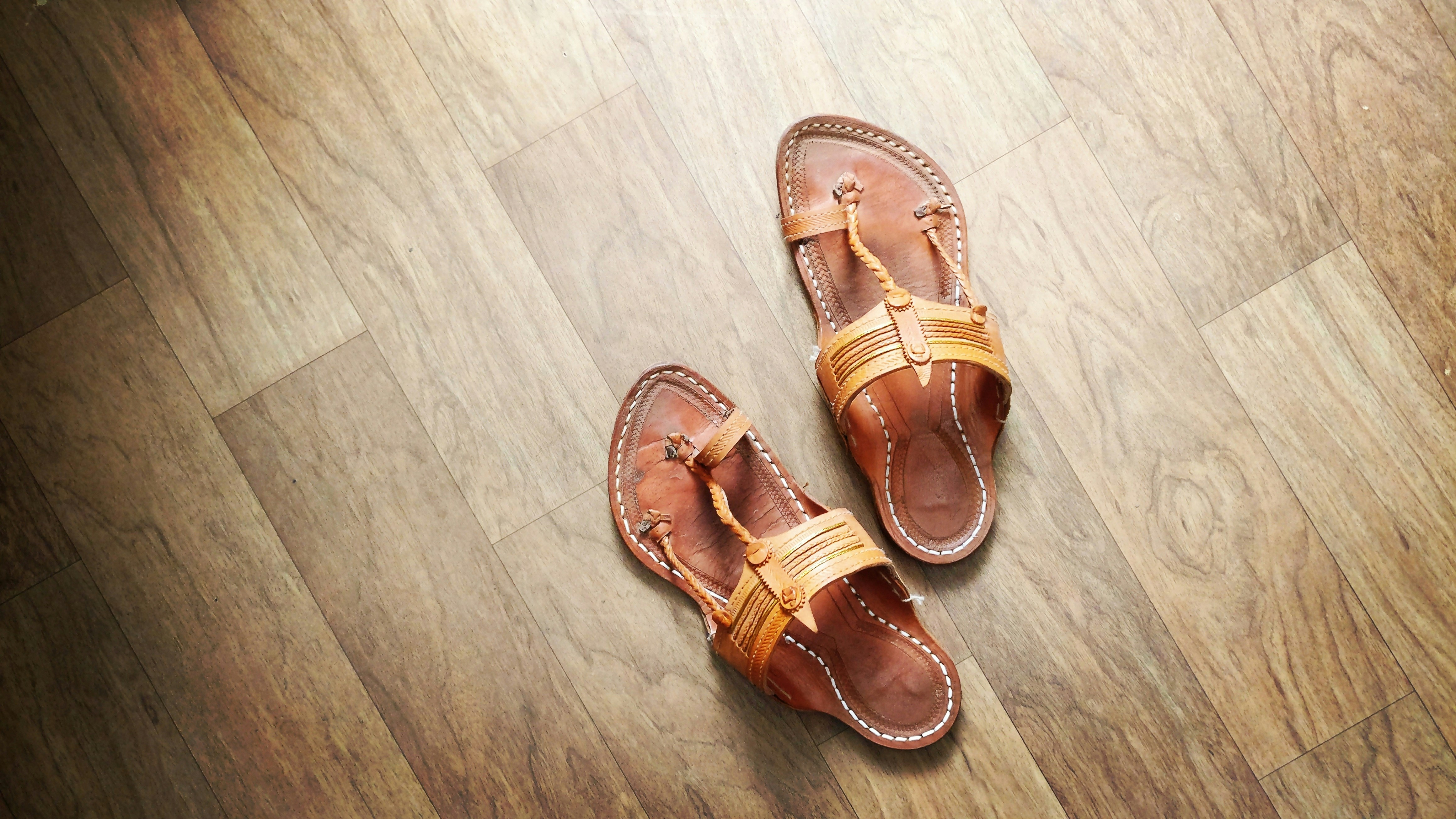Traditional leather sandals on dark wooden floor, warm light
