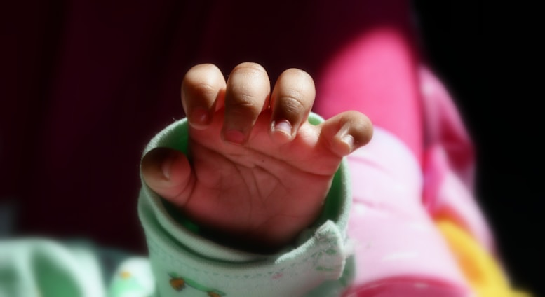 A gentle close-up of a baby wearing a soft pink cloth diaper, smiling and reaching out with tiny hands.