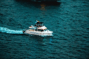 A motorboat navigates through a vast body of water, leaving a visible wake behind it. The name 'MARYTIME' is written on the side of the boat, which has a sleek, white design with additional equipment on the deck.