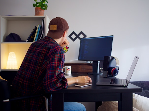 Focused Afro-descendant man coding intently at his desk surrounded by tech equipment.