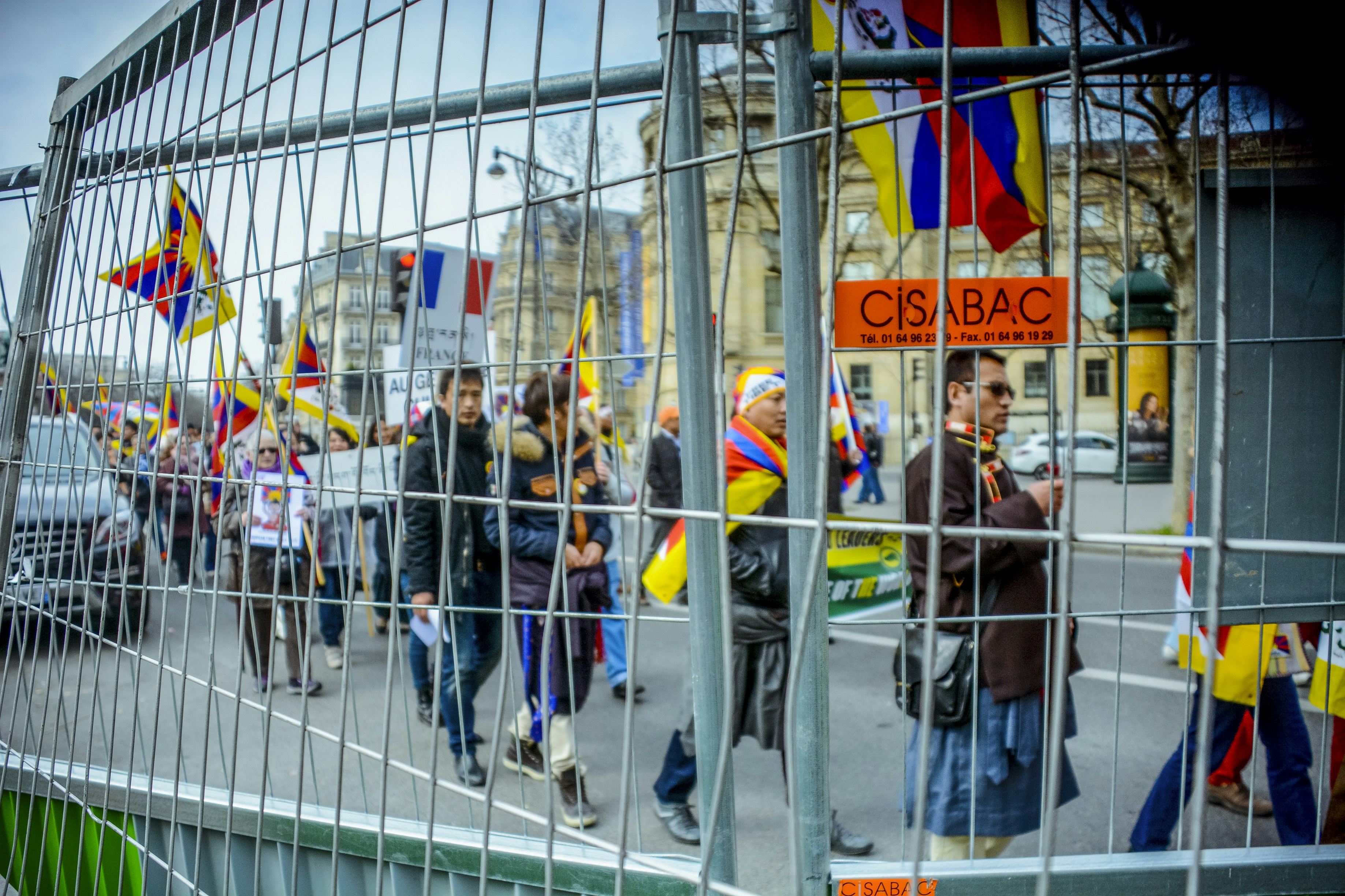 people holding flags and signs walking in line beside gray fence during daytime