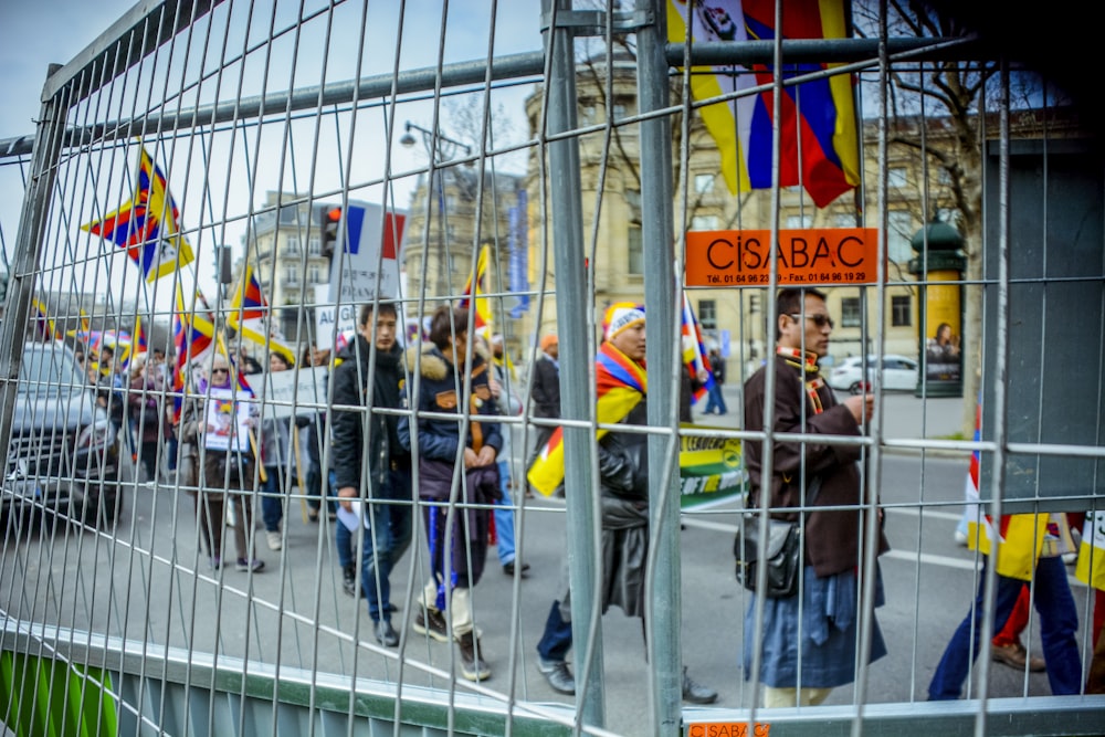 people holding flags and signs walking in line beside gray fence during daytime