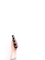 A hand with a tattoo is holding a small, black leather-bound Bible against a stark white background. The Bible's spine is visible, featuring the text 'Holy Bible' and 'NIV.'