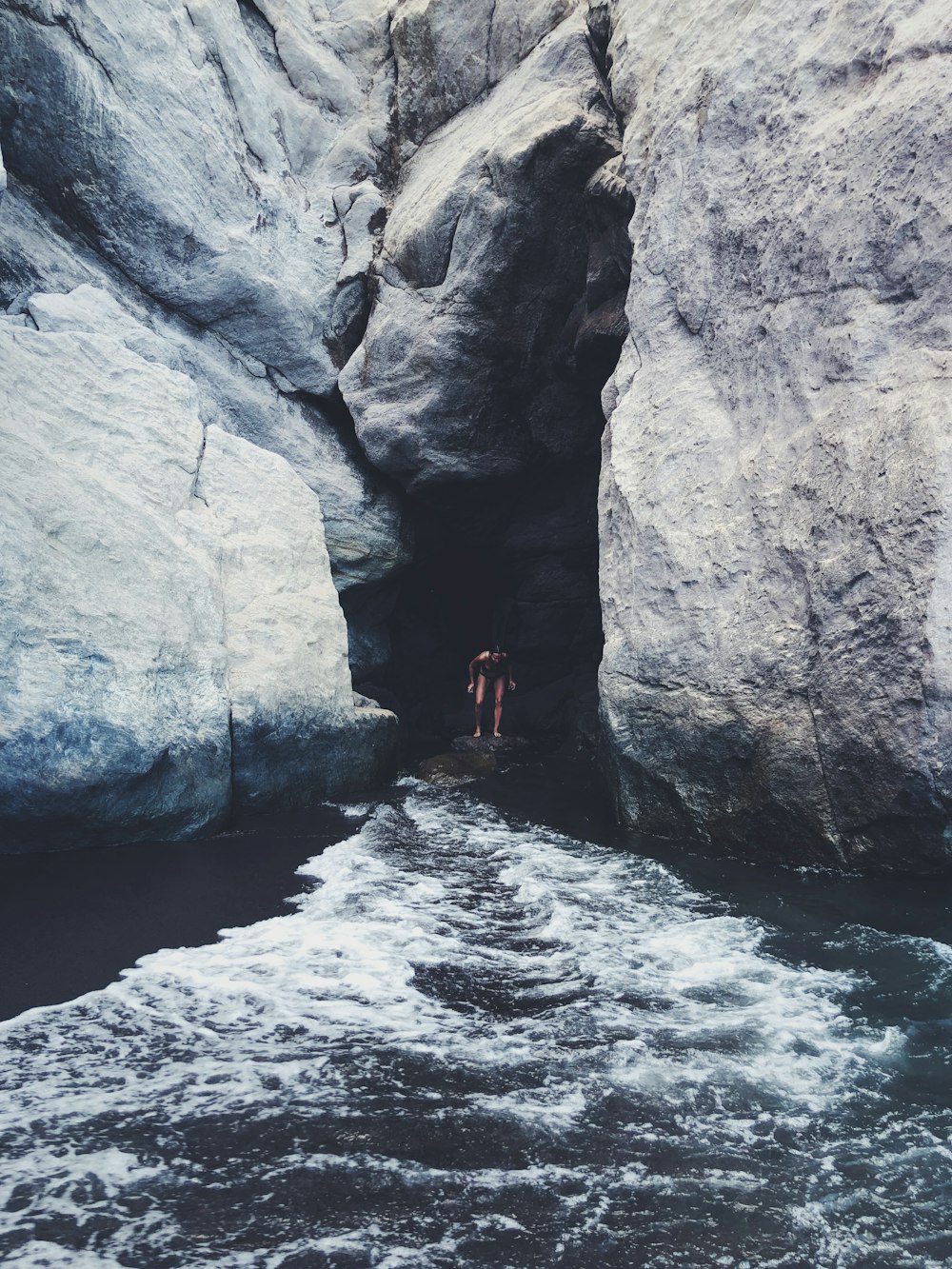 person standing on rock under rock formation near sea during daytime