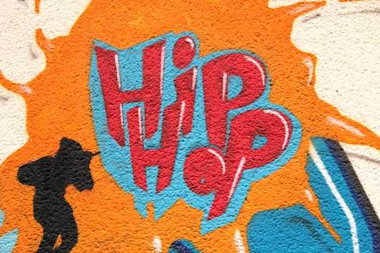 A vivid graffiti design featuring the word 'Hip Hop' in bold red and blue letters, surrounded by an orange splash effect. To the left, a black silhouette of a person holding a microphone adds a dynamic element.