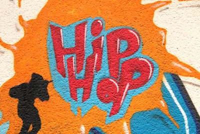 A vivid graffiti design featuring the word 'Hip Hop' in bold red and blue letters, surrounded by an orange splash effect. To the left, a black silhouette of a person holding a microphone adds a dynamic element.