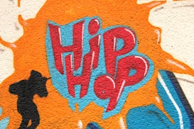 A vivid graffiti design featuring the word 'Hip Hop' in bold red and blue letters, surrounded by an orange splash effect. To the left, a black silhouette of a person holding a microphone adds a dynamic element.