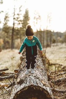 boy wearing jacket walking on tree trunk