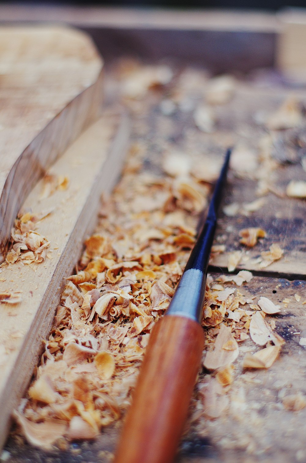brown and black chisel on wood chips beside wood being carved