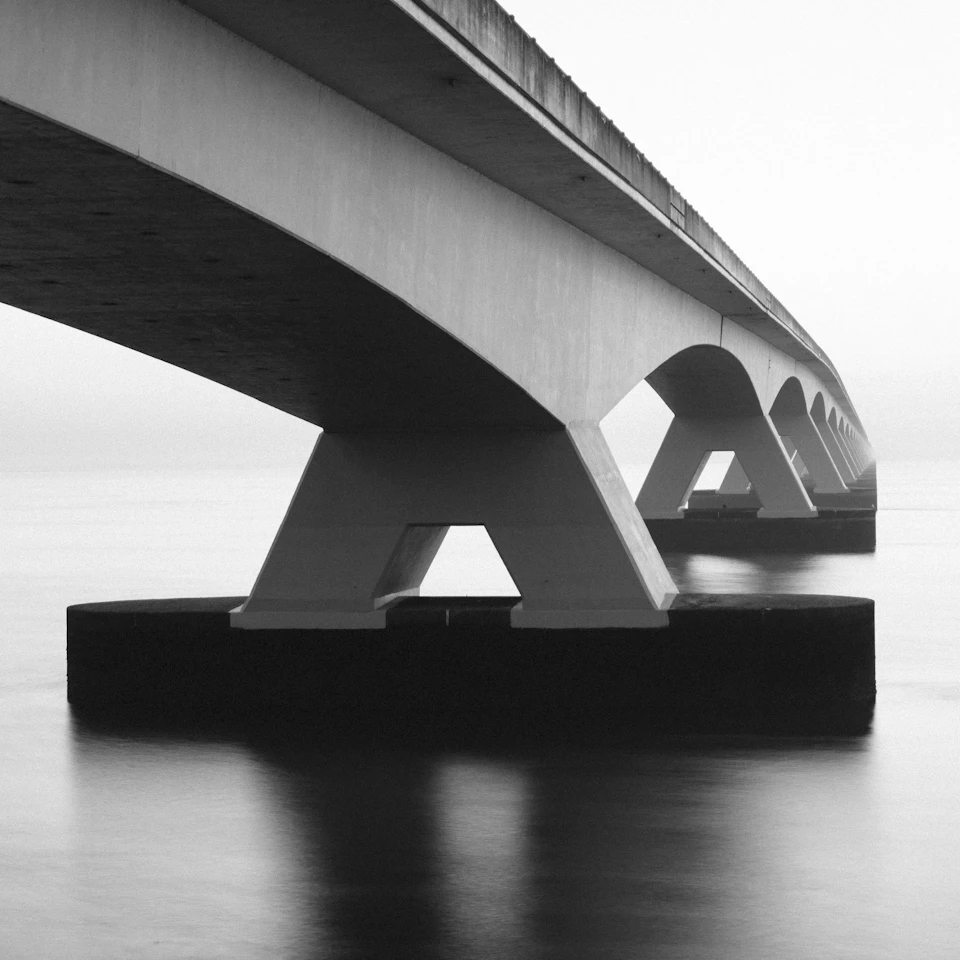 Concrete bridge spanning across water with multiple arches supported by sturdy pillars on either side