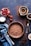 A rustic baking setup featuring a prebaked chocolate crust placed centrally on a dark surface. Surrounding the crust are fresh cherries, some still with stems, in a small dish. A cup of milk and scattered cocoa powder add to the baking theme. Nearby are a sieve with cocoa and a bowl containing liquid chocolate.