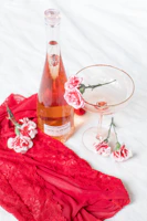 A delicate crimson red rose resting beside a gold-rimmed champagne glass on a white lace tablecloth.