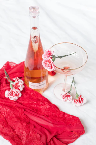 A delicate crimson red rose resting beside a gold-rimmed champagne glass on a white lace tablecloth.
