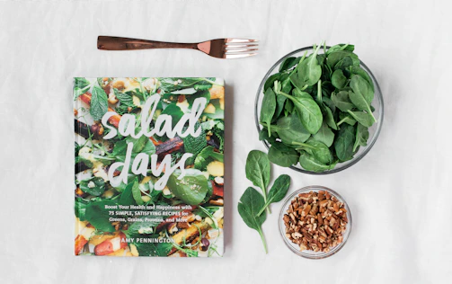 Open recipe book beside a bowl of vibrant salad on a cream linen tablecloth.