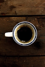 A close-up of a sleek, minimalist mug filled with steaming coffee on a wooden table.