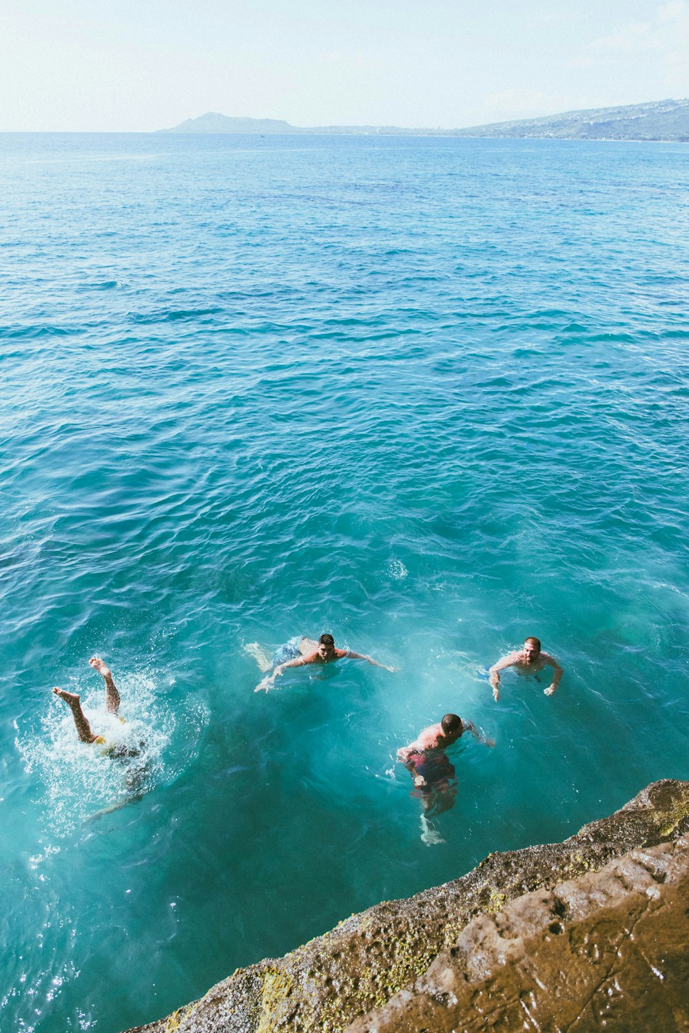 aerial photography of four men swimming in blue sea
