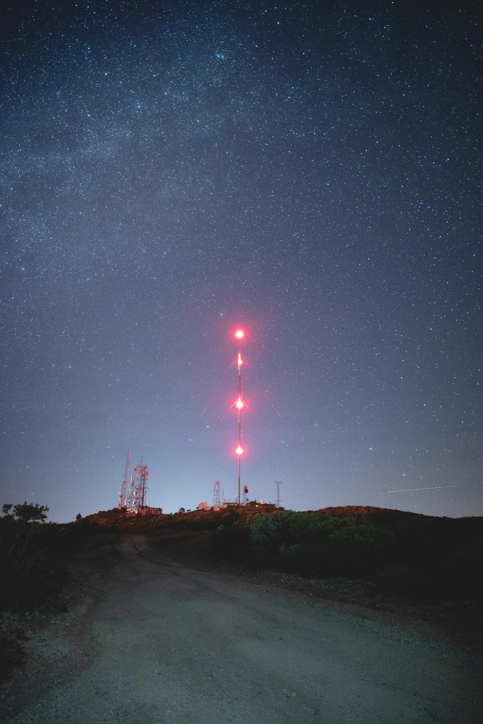 A telecommunications tower with red aviation lights under a starry night sky