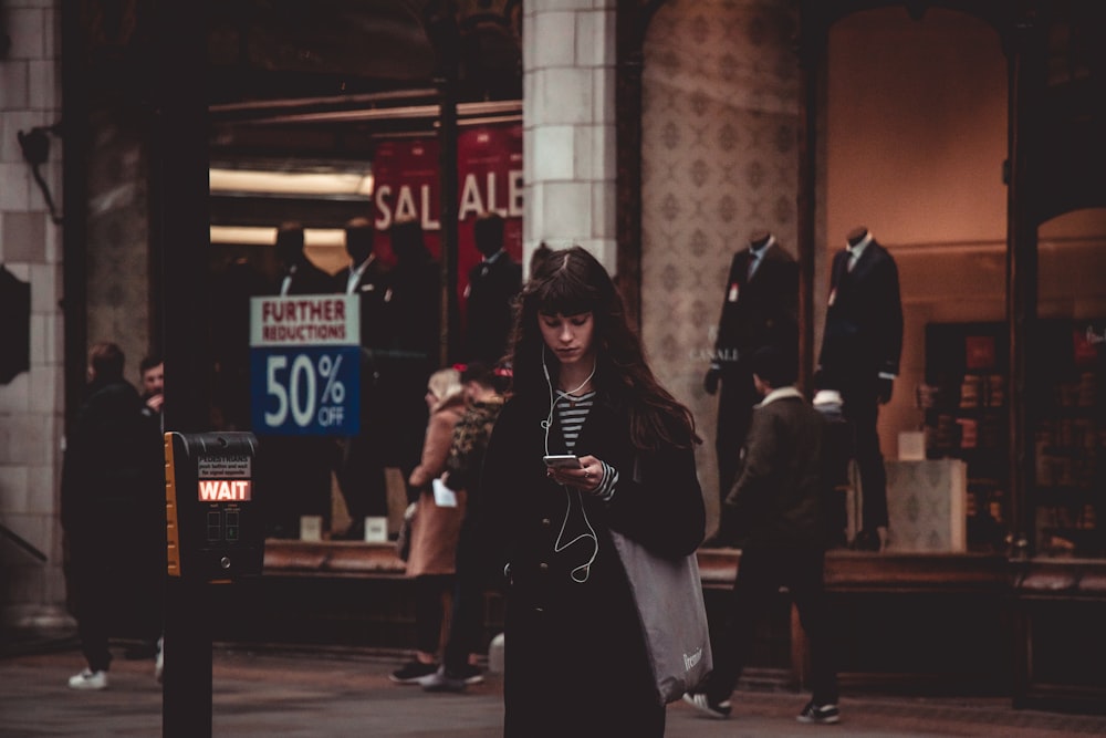 스마트폰과 이어폰을 사용하여 검은 코트를 입고 서 있는 여자