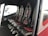 The image depicts the interior of a vehicle featuring a row of four black leather seats with red accents and harness-style seat belts. The seats are aligned side by side on a dark carpeted floor, and there is a window providing an outside view.