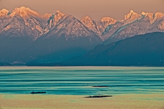 A serene shikara gliding across calm waters with snow-capped mountains in the background.