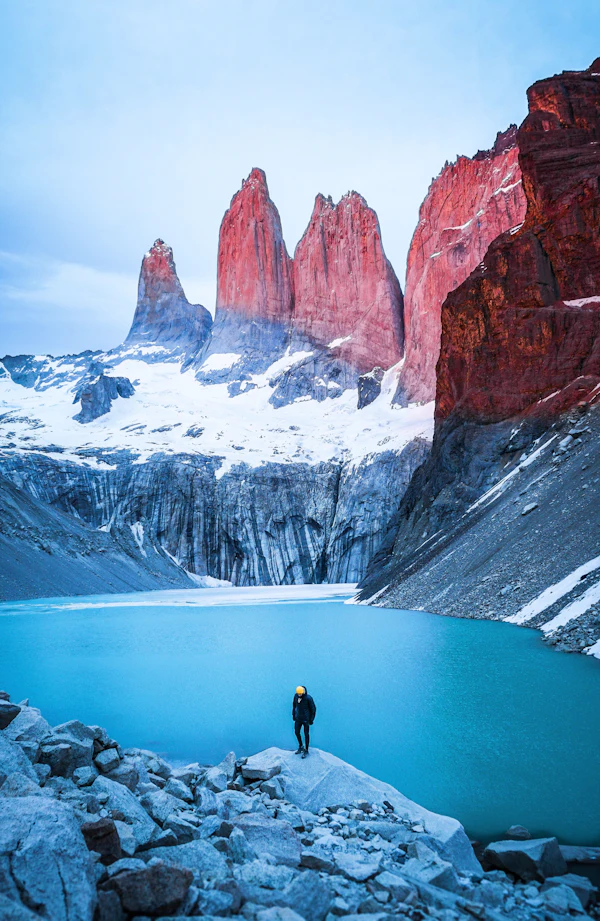 A solitary figure standing on a rock facing distant snow-capped mountains across a still lake