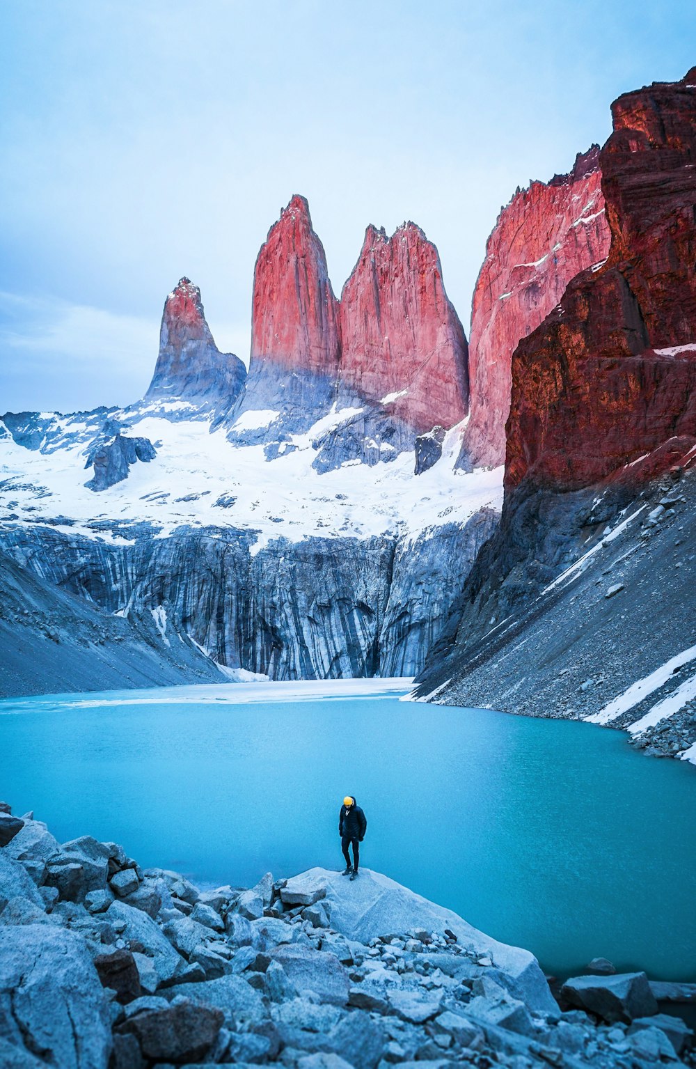 man standing on rock facing body of water and mountain