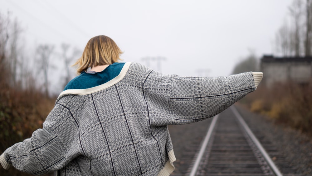 donna in cappotto grigio che cammina sulla ferrovia