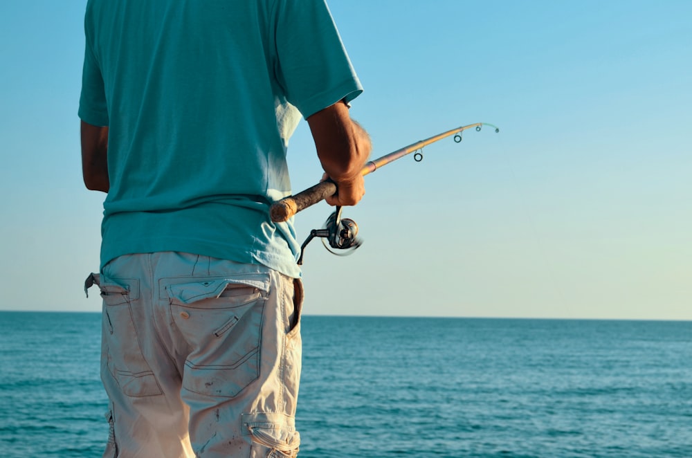 man holding fishing rod facing blue sea