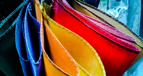 A collection of vibrantly colored fabric pieces arranged in a fan-like pattern. The fabrics are in various shades including blue, purple, red, orange, and yellow. The textures and stitches of the fabrics are clearly visible, creating a rich visual display of colors and materials.