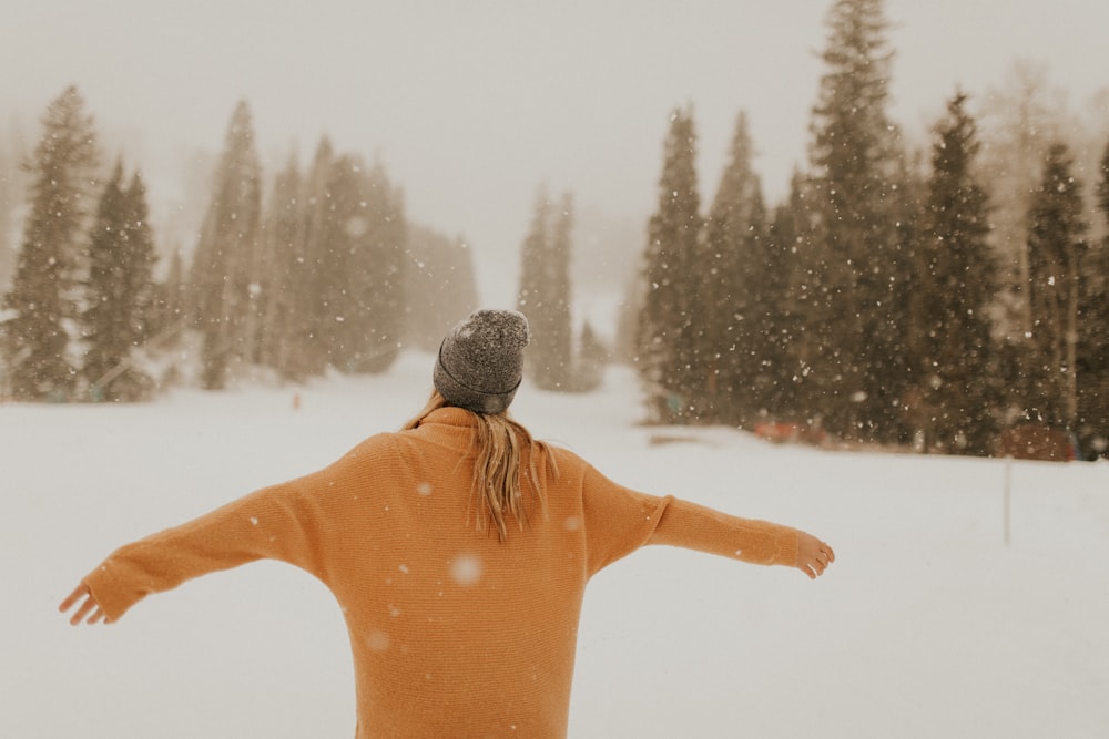 person wearing hoodie while standing on field of snow with arms wide open