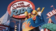 A vibrant amusement park ride featuring cartoon characters in a roller coaster cart beneath a large, colorful sign. The characters appear animated and joyful, with exaggerated facial expressions. The surroundings include bright, playful architecture and additional amusement park elements.