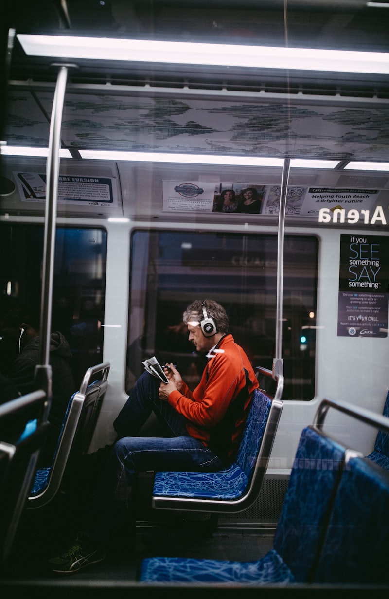 Senior man wearing headphones while reading on a train, enjoying audiobooks during his commute