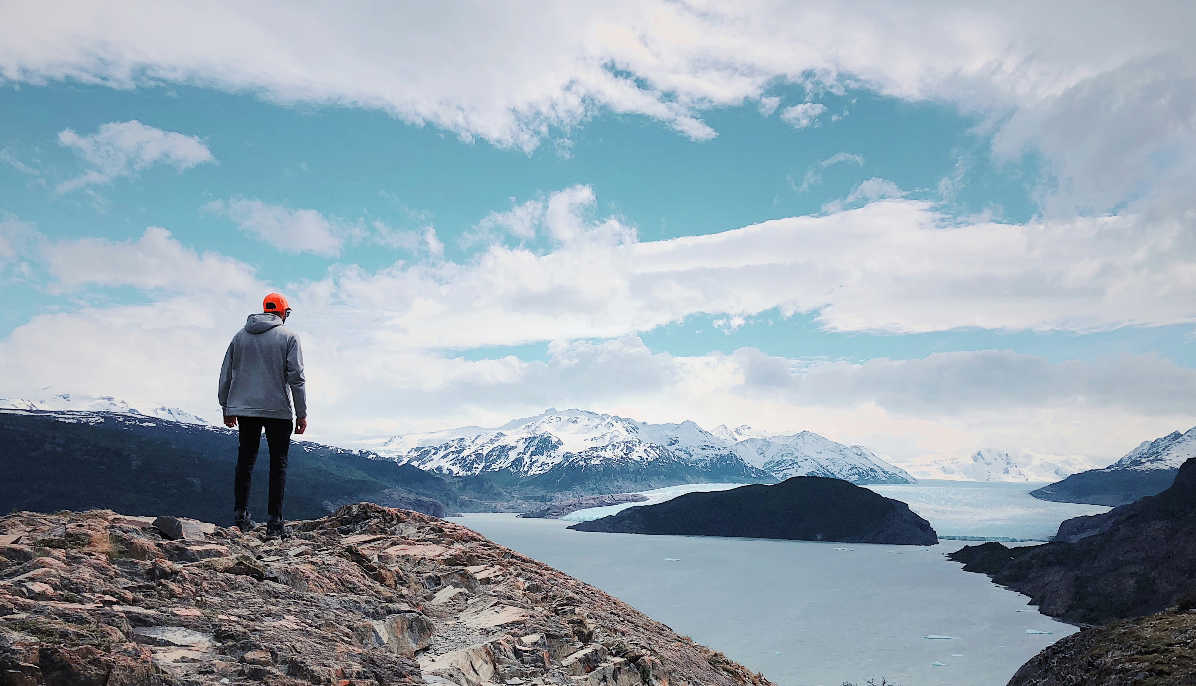 person in gray jacket and black pants standing on cliff looking over at water