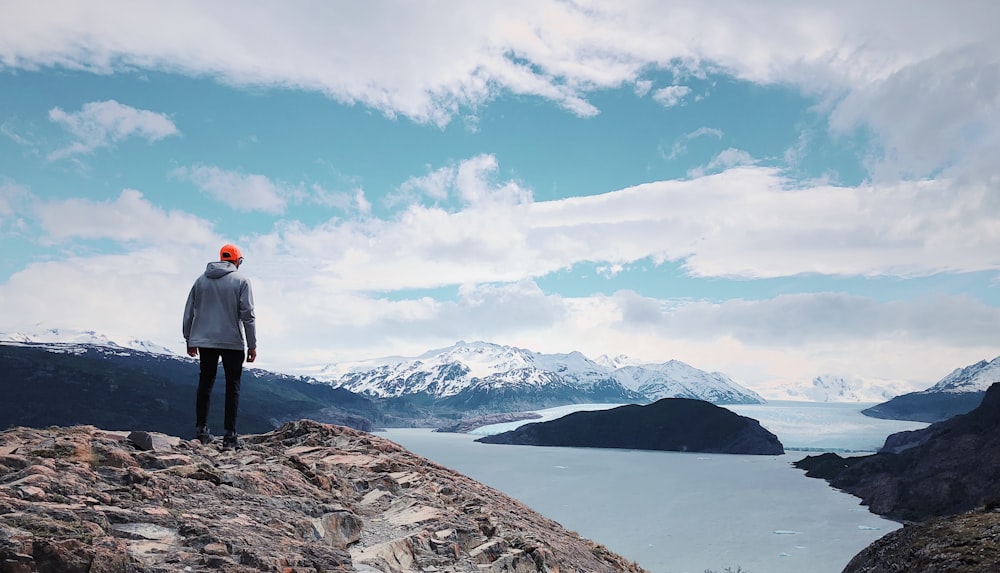 person in gray jacket and black pants standing on cliff looking over at water