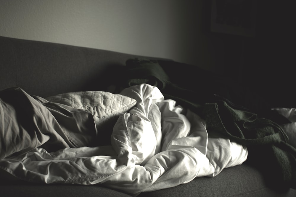 grayscale photography of crumpled blankets on sofa