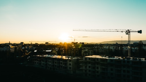 A city skyline at sunset showcasing modern skyscrapers and construction cranes.