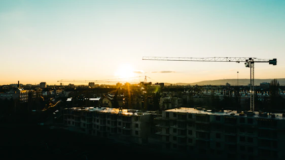 A modern urban skyline at sunset with cranes and new buildings showcasing construction in progress.