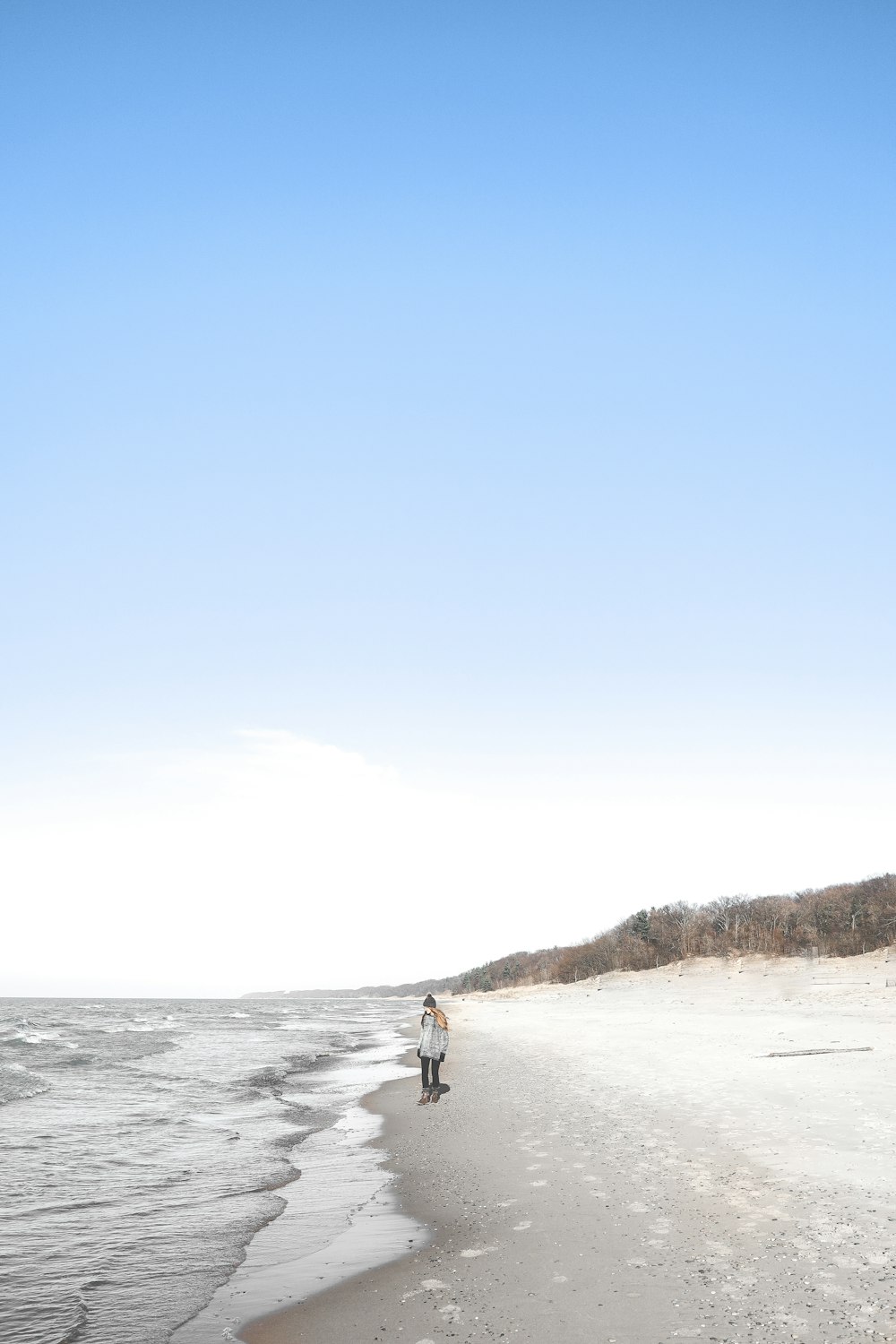 person standing on beach sand near sea water