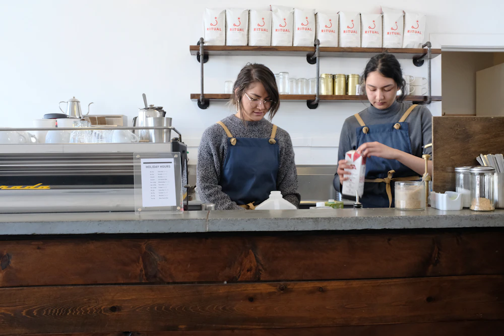 Two people in aprons preparing drinks behind a counter