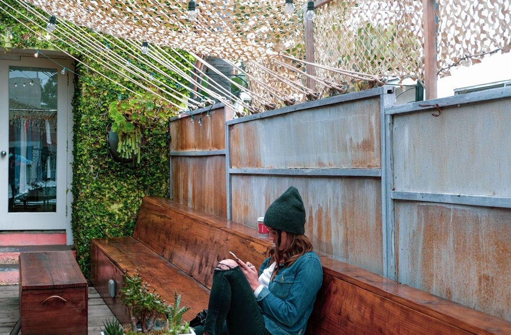 woman sitting on bench while using phone during daytime