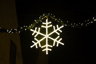 A glowing LED snowflake decoration hanging on a building facade at night