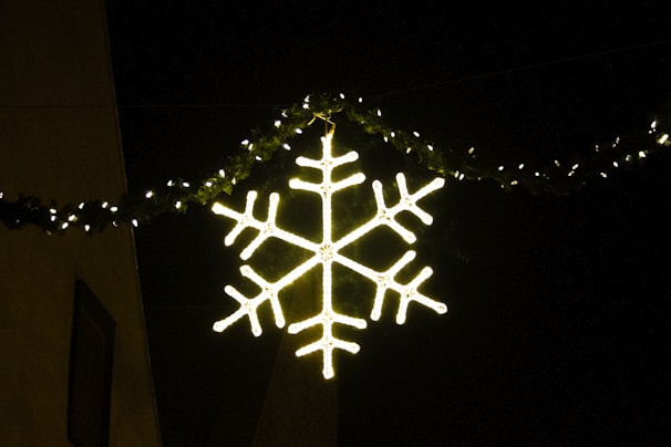 A glowing LED snowflake decoration hanging on a building facade at night