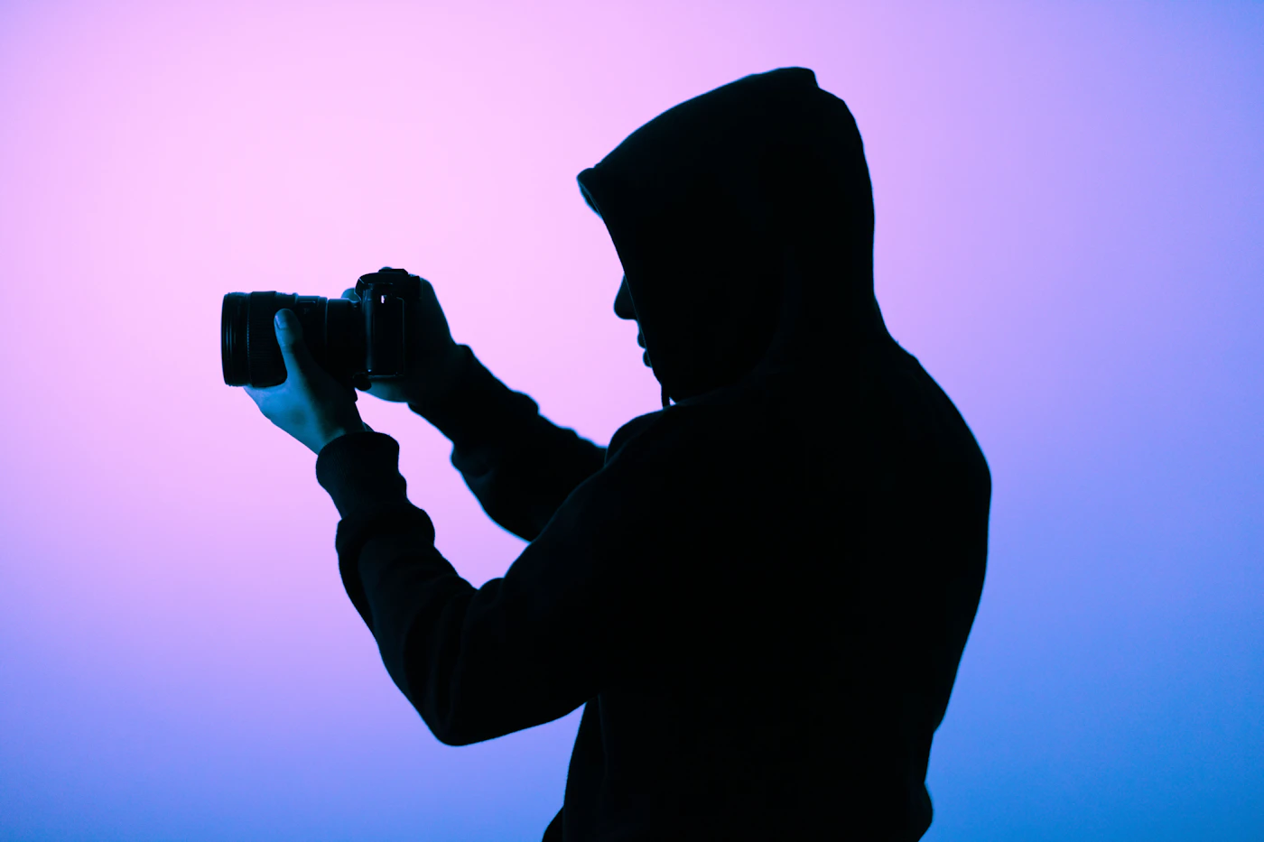Silhouette of a person holding a camera up to shoot, backlit by blue and violet light