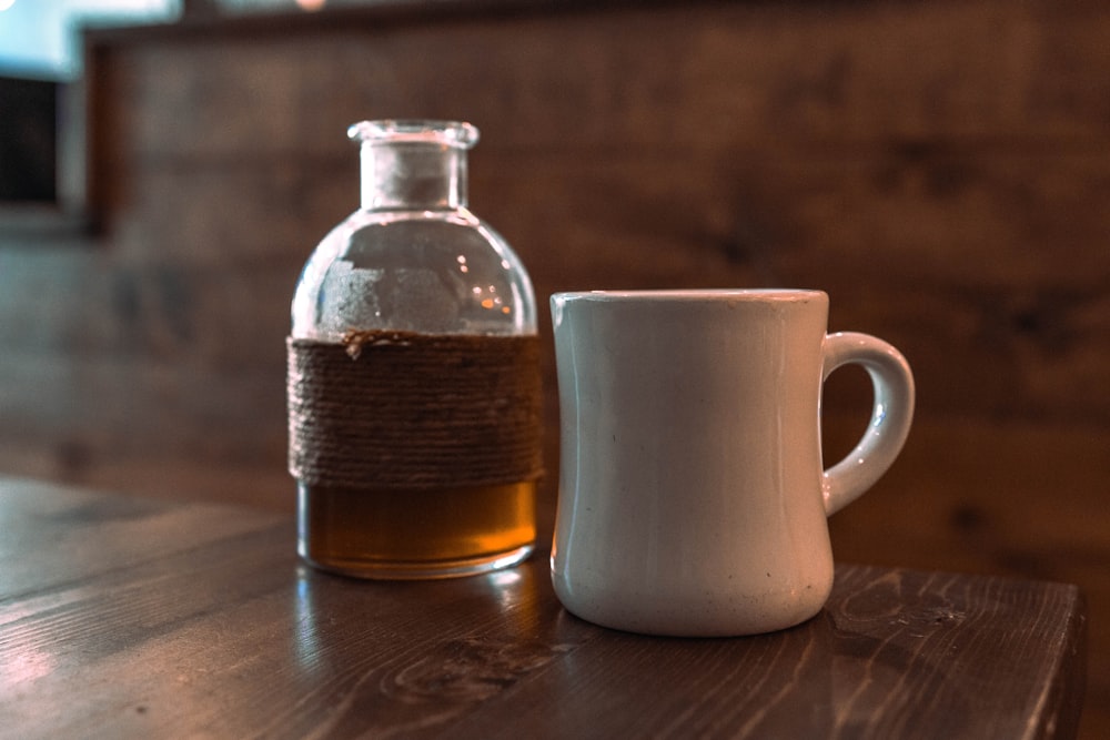 white ceramic mug beside clear glass bottle