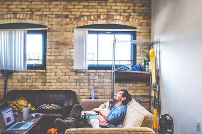 Relaxed man sitting on a couch with his dog, surrounded by warm, pastel home decor.