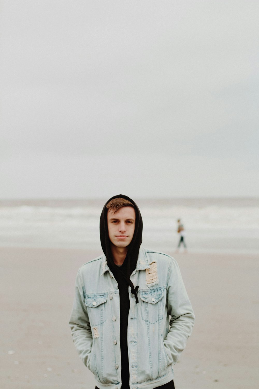 Homem em pé na praia com as duas mãos nos bolsos do casaco