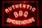 Bright neon letters spell out 'Authentic BBQ Smokehouse' in a vivid red color on a dark background. The signage is enclosed in a glass frame and illuminated, creating a warm, inviting glow.