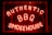 Bright neon letters spell out 'Authentic BBQ Smokehouse' in a vivid red color on a dark background. The signage is enclosed in a glass frame and illuminated, creating a warm, inviting glow.