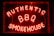Bright neon letters spell out 'Authentic BBQ Smokehouse' in a vivid red color on a dark background. The signage is enclosed in a glass frame and illuminated, creating a warm, inviting glow.